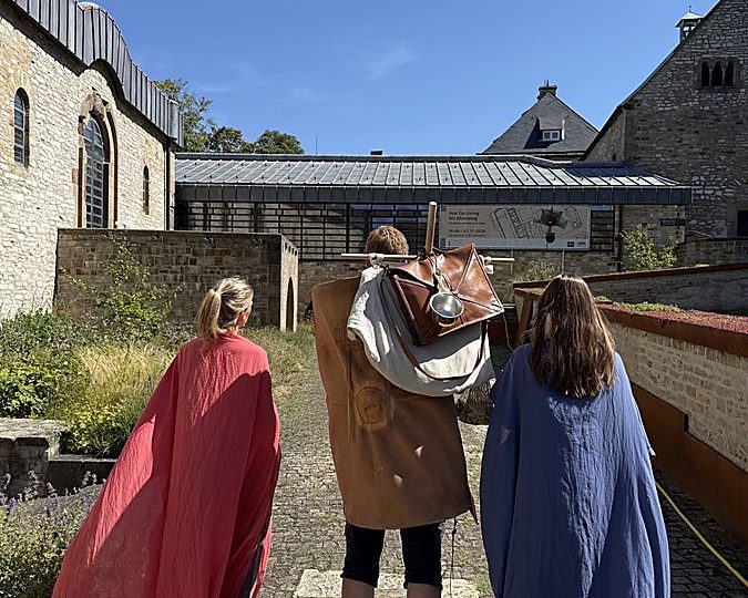 Drei Personen in römisch anmutenden Gewändern stehen im Innenhof des LWL-Museums in der Kaiserpfalz in Paderborn.Drei Personen in römisch anmutenden Gewändern stehen im Innenhof des LWL-Museums in der Kaiserpfalz in Paderborn.